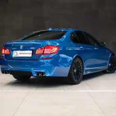 Niebieskie BMW M5 F10 z czterema końcówkami wydechu i czarnymi felgami, gotowe do jazdy.